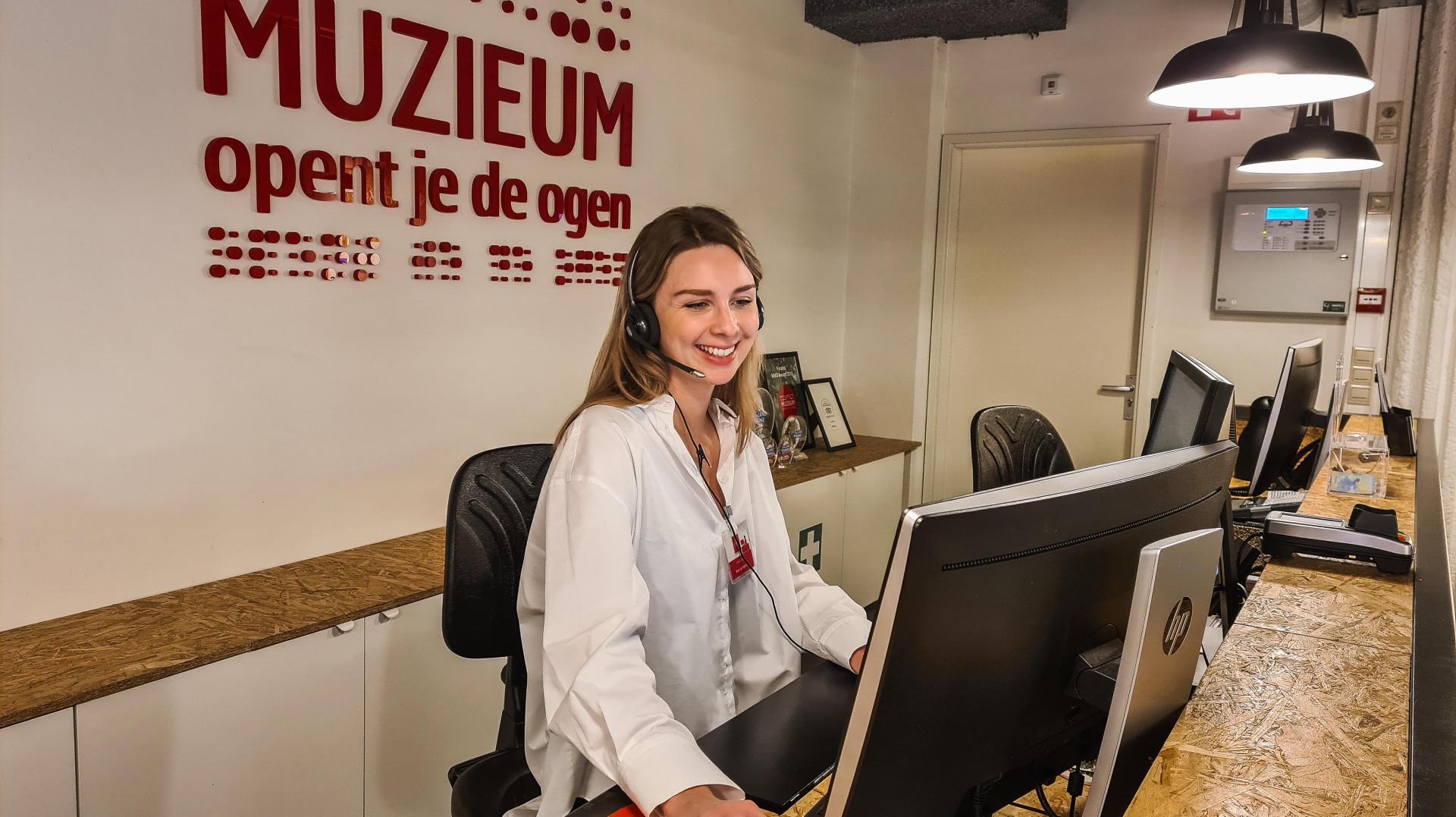 Medewerker achter de balie met headset op, achter haar muZIEum logo